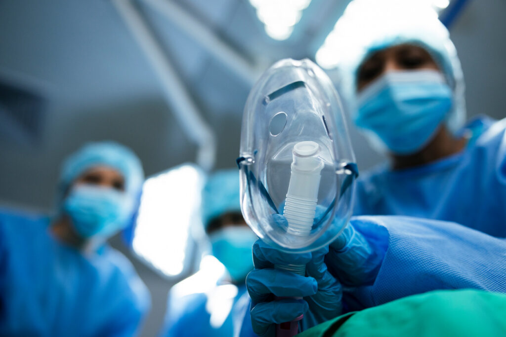 Low angle, surgeon and oxygen mask for surgery in operating room, doctors and anesthesia with pov. Perspective, equipment for medical procedure and gas, treatment and people in theater for health
